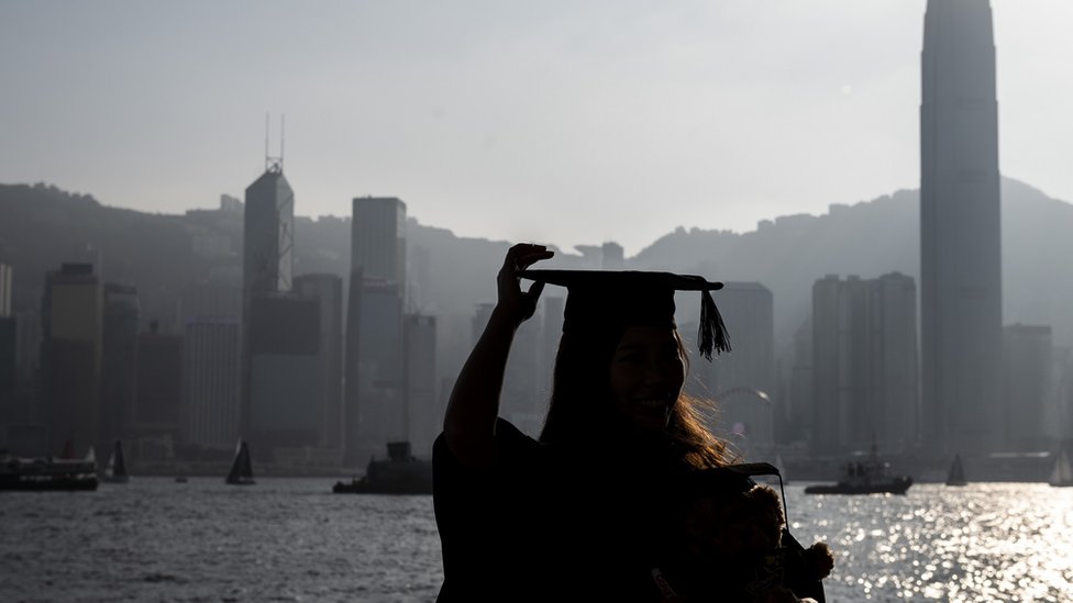 A women wearing a graduation gown posing for a photo in front of the Hong Kong Skyline on November 20, 2022 in Hong Kong, China. (Photo by Vernon Yuen/NurPhoto via Getty Images)