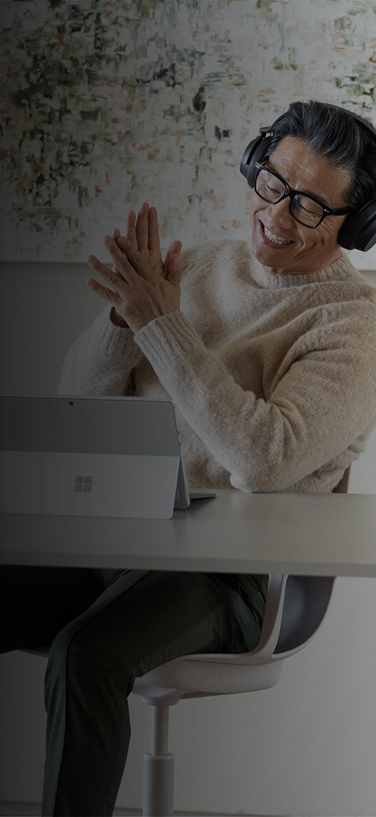 Un hombre sentado en su oficina en casa disfruta de su Surface Pro 9 con Surface Headphones 2+