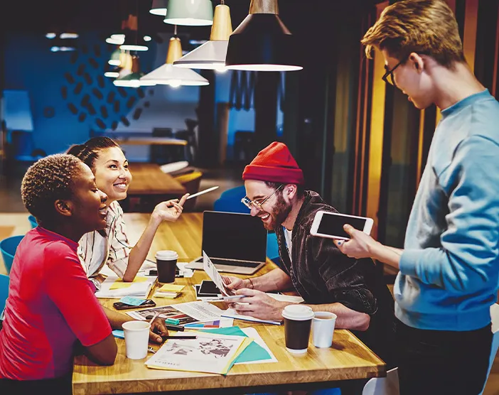 Ein fröhliches, diverses Team sitzt an einem Tisch in einem Co-Working Space und tauscht Ideen aus.