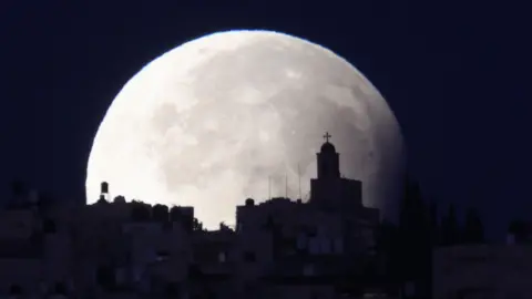 A supermoon with a partial lunar eclipse sets over the old city of Jerusalem, 18 September 2024.