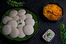 Sepiring idli berwarna terang di sebelah semangkuk sambar