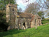 Yellow stone building with square tower, surrounded by trees.