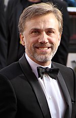 A middle aged man wearing a tuxedo faces forward while smiling.