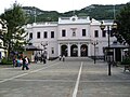 A long plaza with a large two—storey pink building at the far end, with a flight of steps leading up to the building's triple—arched entrance framed with columns.