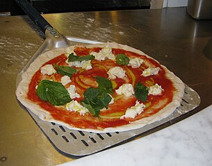 An uncooked Neapolitan pizza on a metal peel, ready for the oven