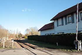 Quais (dont un est recouvert par la végétation), voie unique et ancien bâtiment voyageurs, vus depuis le passage à niveau voisin.