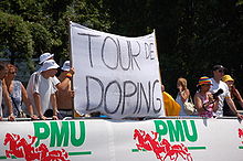 Photographie couleur montrant des spectateurs portant une banderole avec l'inscription en noir sur fond blanc : « Tour de doping ».