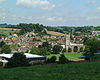 multiple buildings including a square church tower amongst fields and trees.