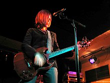 A worm's eye-view of a Caucasian woman with medium-length brunette hair playing guitar