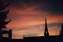 Ombres d'un bâtiment et d'un clocher se détachant en noir sur ciel rouge d'un soleil couchant.