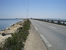 Perspective sur une route aménagée sur une digue entourée de part et d’autre par la mer ; un pipeline a été aménagé du côté droit.