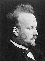 A middle-aged man with a small pointed beard and black bow-tie in profile