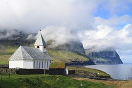 Viðareiðis kirkja med utsikt mot høye klipper. Foto: Dreizung