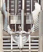 A stylized figure of a male human with outstretched arms and head tilted slightly forward, wearing a winged and crested helmet, mounted on the facade of a building