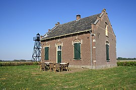 Photographie en couleurs d'une maison au milieu d'un espace de verdure et d'un phare en arrière-plan