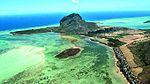 An aerial view of a sandspit, home to a large, pointy boulder. Shallow water surrounds its sides, while the sea covers its backside.