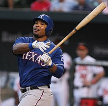 A man in a blue baseball helmet and a blue baseball jersey swinging a blond wooden bat