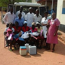 Un groupe de personnes, dont un nouveau-né, pose devant un véhicule sanitaire.