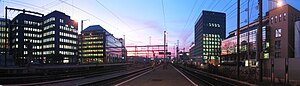 Railroad tracks surrounded by lit office buildings as the sun sets below the horizon