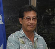 Front portrait of the President in a blue shirt with white and green plant motifs