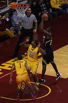 Player shooting a layup, guarded by two opponents