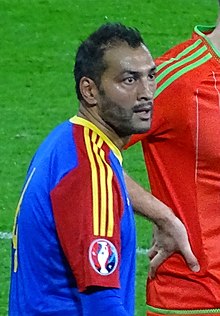 A man with dark hair wearing a red, blue and yellow jersey.