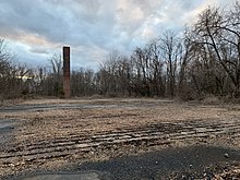 A once used chimney now stands alone next to a previously demolished building's cement foundation.