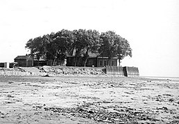 Photographie en noir et blanc de terres vierges et d'une butte surmontée par des bâtiments et des arbres en arrière-plan