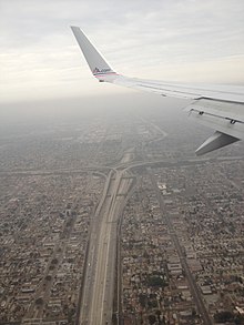 On voit l'aile d'un avion en haut de l'image, l'échangeur en bas avec de part et d'autre des habitations.