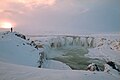 Coucher de soleil hivernal sur les chutes enneigées de Goðafoss, en Islande.