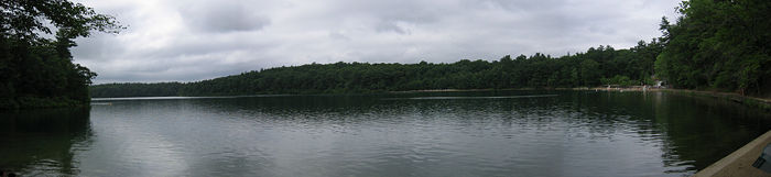 Vue panoramique de l'étang de Walden en juillet 2005 entouré de ses bois. À droite de l'image se distinguent une berge artificielle et des installations de loisir.