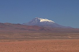 A snow covered flat-conical mountain rises above a ridge