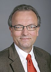 Portait d'un homme aux cheveux gris, portant des lunettes.