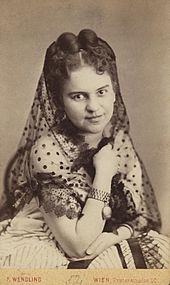 Photographie d'une jeune femme aux cheveux épinglés, portant une robe blanche et un foulard partiellement transparent.