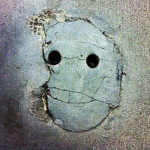 A 'Concrete smiley face', this is actually 2 holes in the ground for holding 2 chain link fence doors at a Lowes Construction supply store in San Francisco.