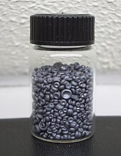 A small glass jar filled with small dull grey concave buttons. The pieces of selenium look like tiny mushrooms without their stems.