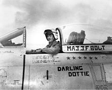 A man in a flight suit and helmet sits in the cockpit of an aircraft