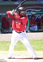 Batter in black hat red top and white pants, batting during spring training for the Red Sox.