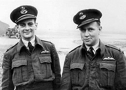 Informal half portrait of two men in dark military uniforms, with peaked caps