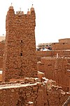 A picture of a tall stone and medieval looking tower, surrounded by buildings constructed with the same material.