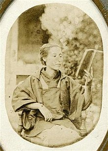 Monochrome photograph of an elderly Kusumoto Ine seated and reading a book