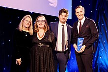 Colour photograph of members the ITV News team posing onstage with their AIB award.