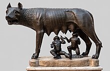 Statue en bronze d'une louve avec deux enfants en dessous qui la têtent.