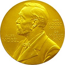 A golden medallion with an embossed image of a bearded man facing left in profile. To the left of the man is the text "ALFR•" then "NOBEL", and on the right, the text (smaller) "NAT•" then "MDCCCXXXIII" above, followed by (smaller) "OB•" then "MDCCCXCVI" below.